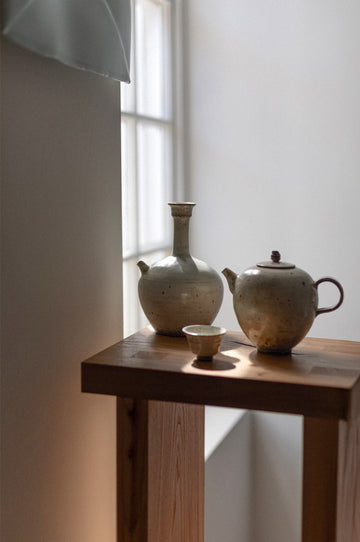 Ceramic teapot, vase, and small bowl on a wooden table with a soft light background